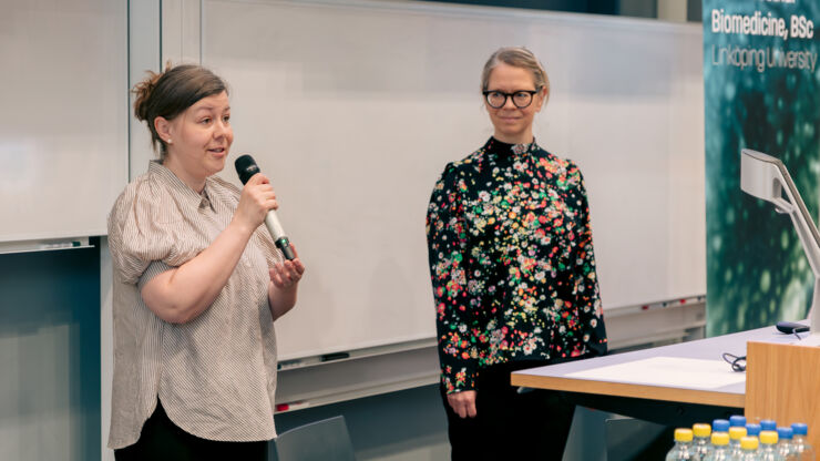 Two women in a lecture hall with a powerpoint presentation in the background.