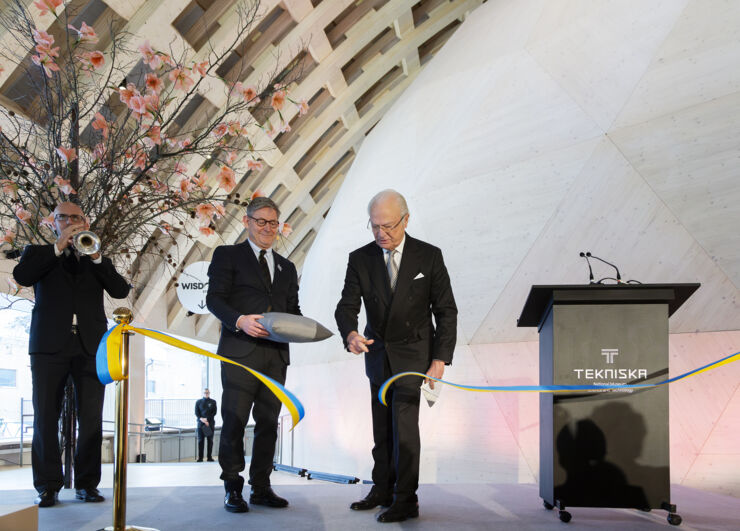 A man (king Carl XVI Gustaf) cuts a blue and yellow ribbon inside a dome theatre