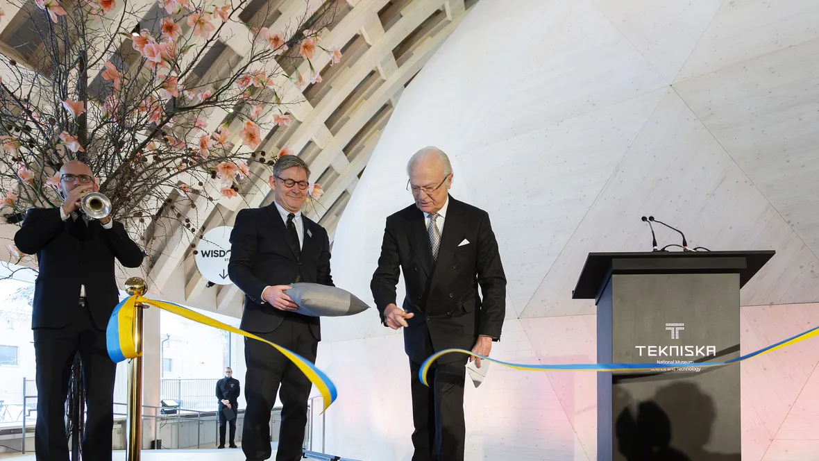 A man (king Carl XVI Gustaf) cuts a blue and yellow ribbon inside a dome theatre