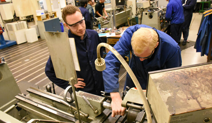 Två ingenjörsstudenter lär sig svarva i metall för bättre förstå processen vid metallbearbetning.