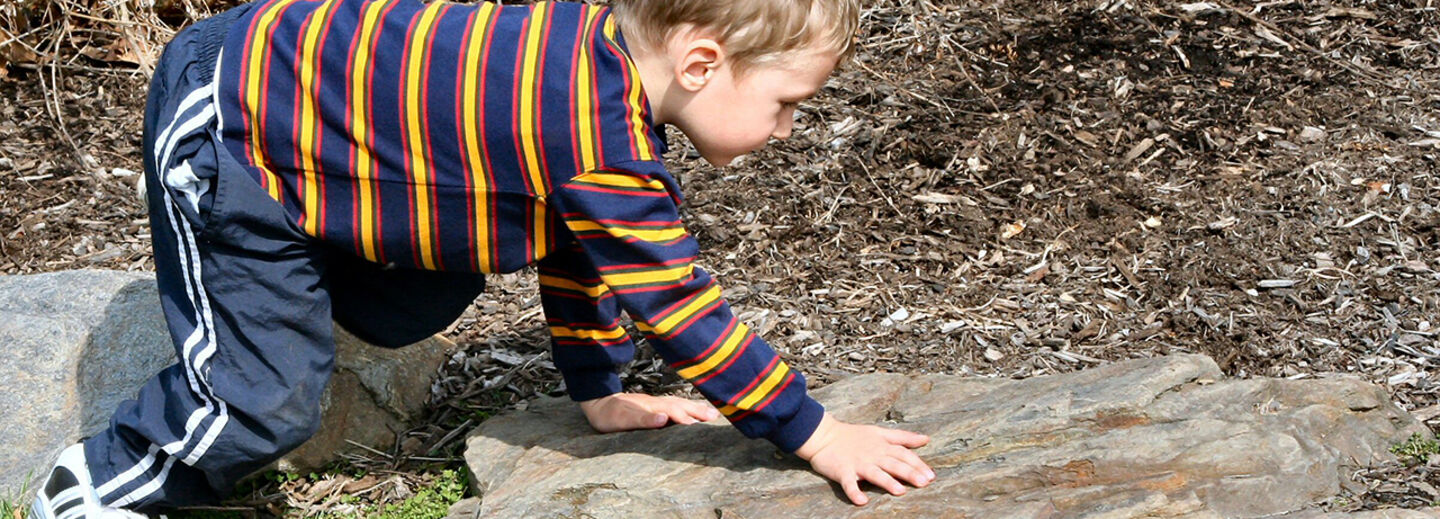 A little boy playing on a rock. 