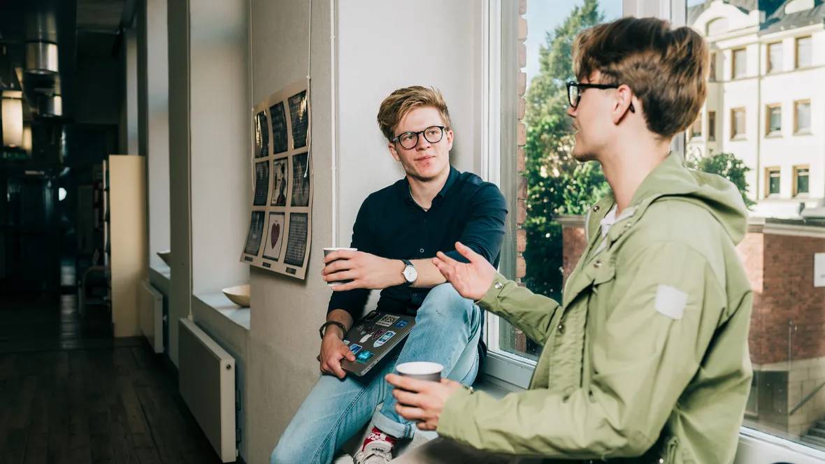 Två manliga studenter som sitter i ett fönster och samtalar
