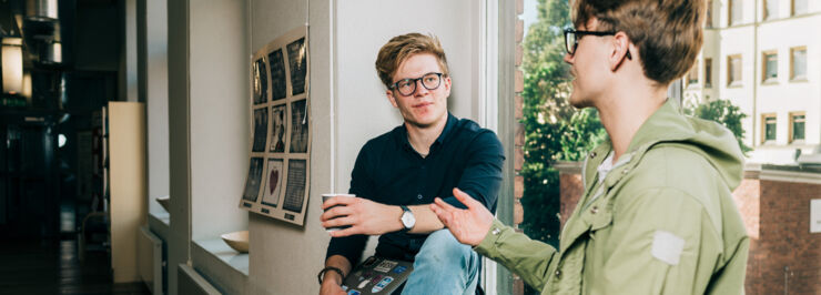 Two male students talking sitting in a window