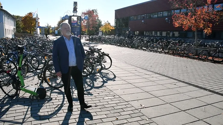 En man står framför en rad cyklar, omgiven av en urban miljö.