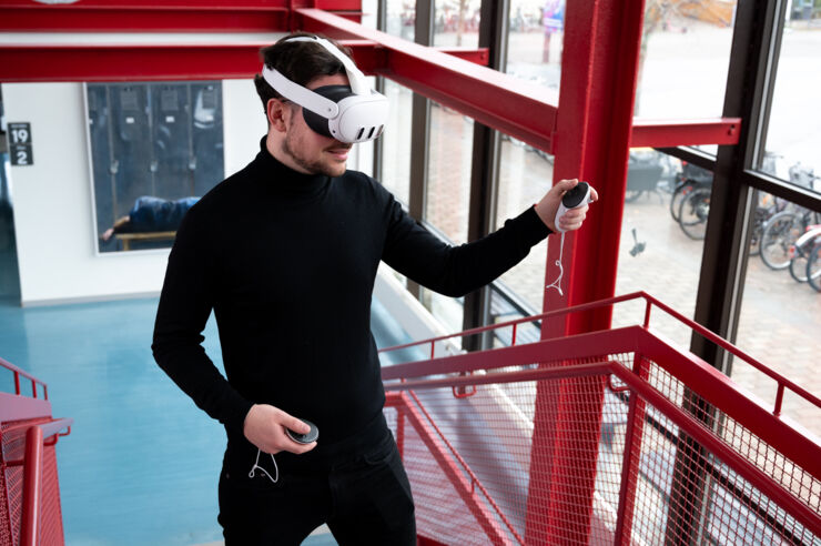 A man wearing a virtual reality headset stands on a stairwell, immersed in a digital experience.