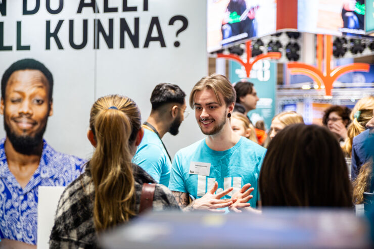 LiU-student med turkos t-shirt pratar med besökare på mässa