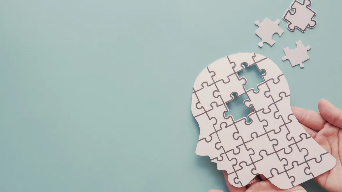 En hand som håller i ett pussel i form av ett människohuvud.