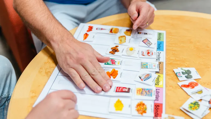 Två personer tar fram ett bildbaserat veckoschema.