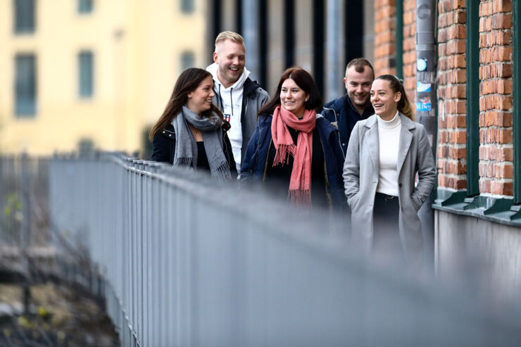 Fem studenter går på en gångbro bredvid en tegelbyggnad.