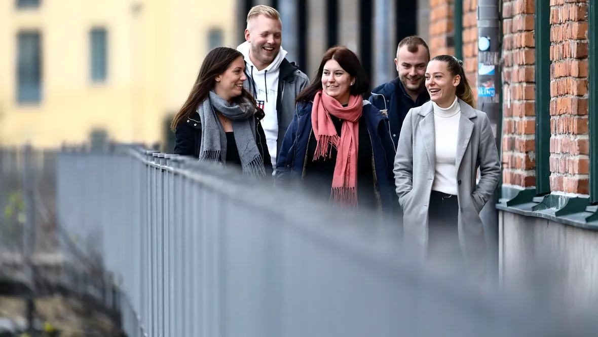 Fem studenter går på en gångbro bredvid en tegelbyggnad.