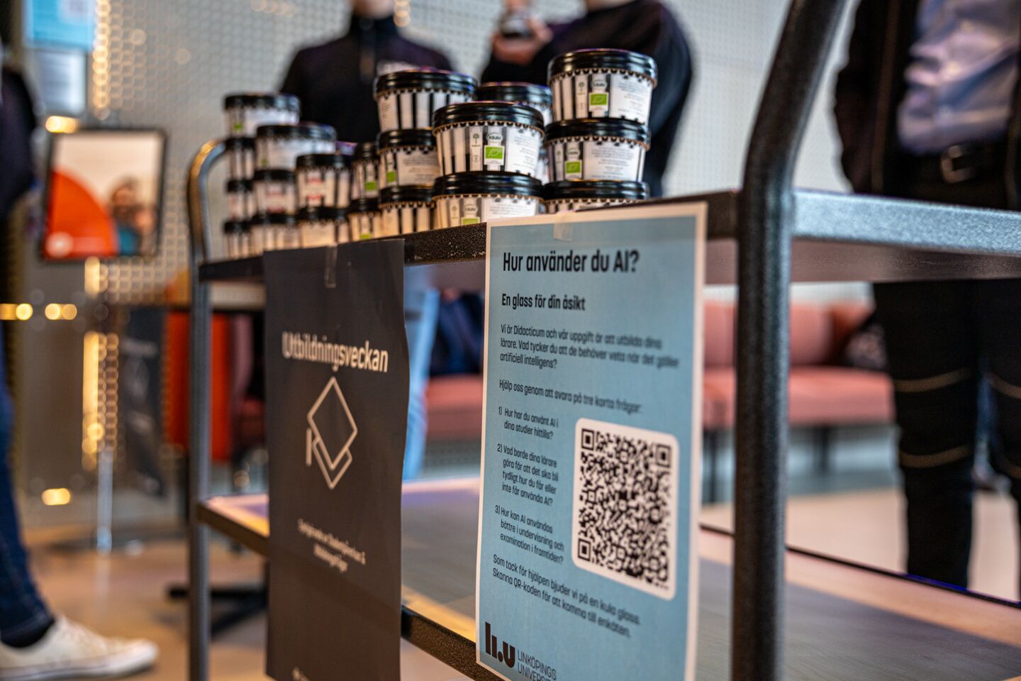 Skylt med QR-kod och information, glass i bakgrunden.