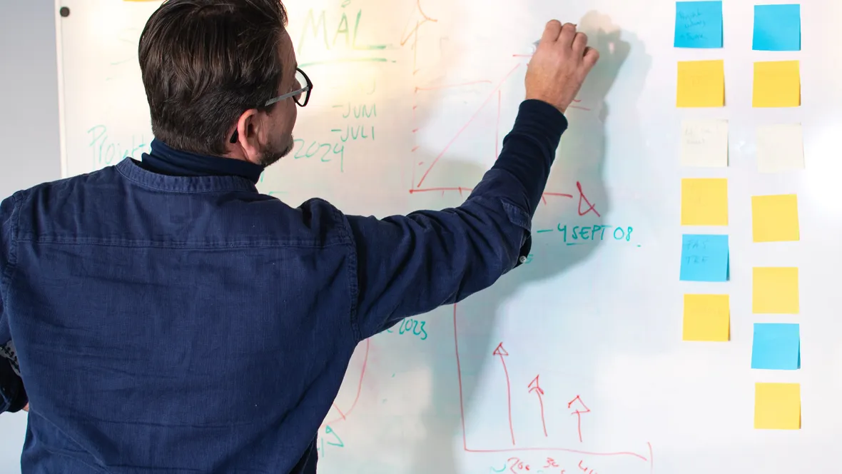 Man framför whiteboard med penna i hand, redo att skriva. 