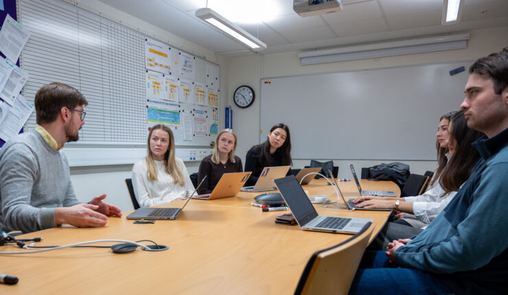 En grupp människor sitter runt ett bord med bärbara datorer, engagerade i diskussioner och arbete.