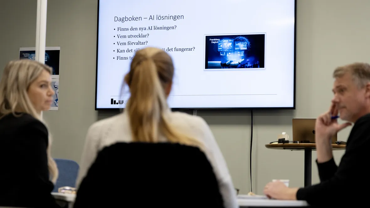 Tre vuxna studenter diskuterar AI i ett klassrum.